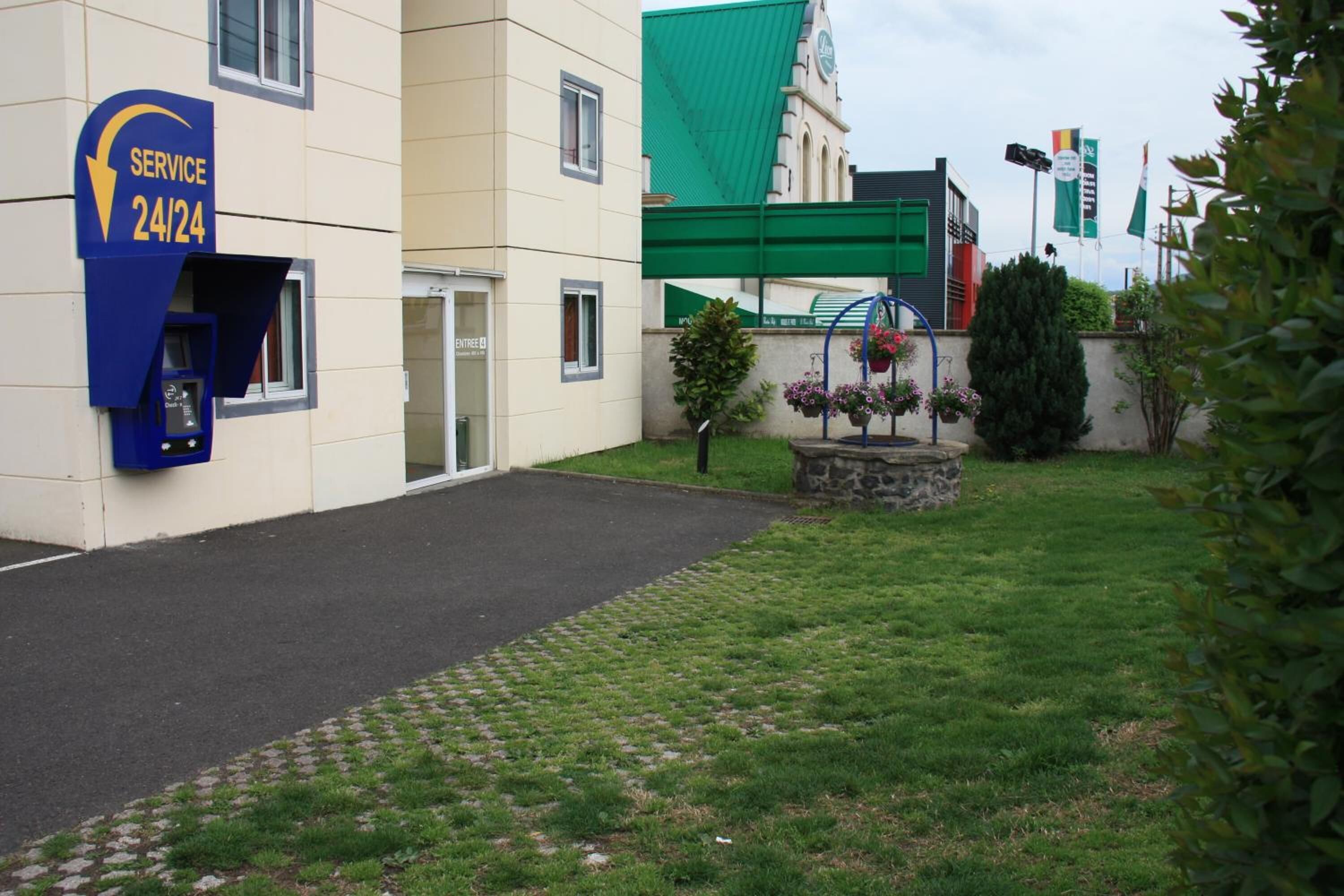 Un edificio con un letrero que indica servicio 24 horas, un toldo verde y una jardinera de piedra con flores.