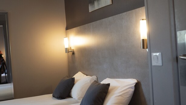 A hotel room with two beds, each with white and dark gray pillows, and two wall-mounted light fixtures.