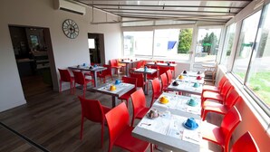 A restaurant with red chairs and tables, a clock on the wall, and large windows.