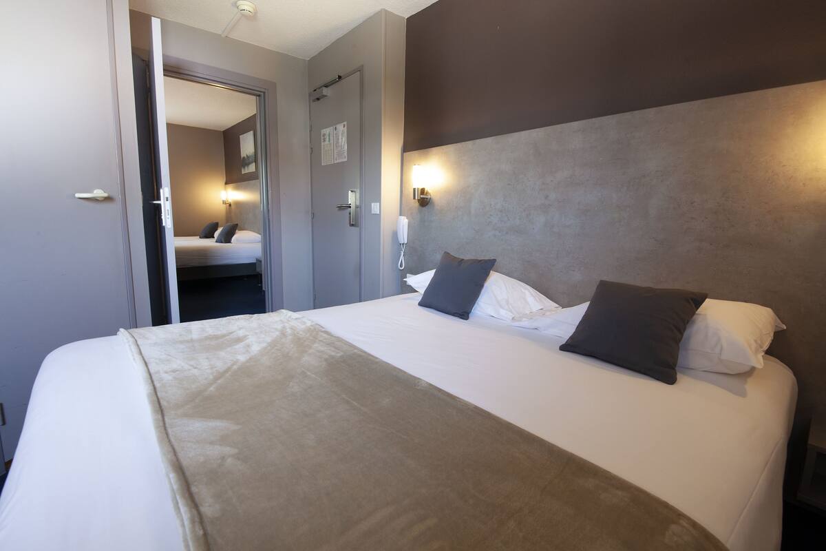 Une chambre d’hôtel avec un lit, un téléphone sur la table de chevet et une porte donnant sur une autre pièce.