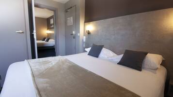 Quarto de hotel com cama, telefone de mesa e porta para outro cômodo.