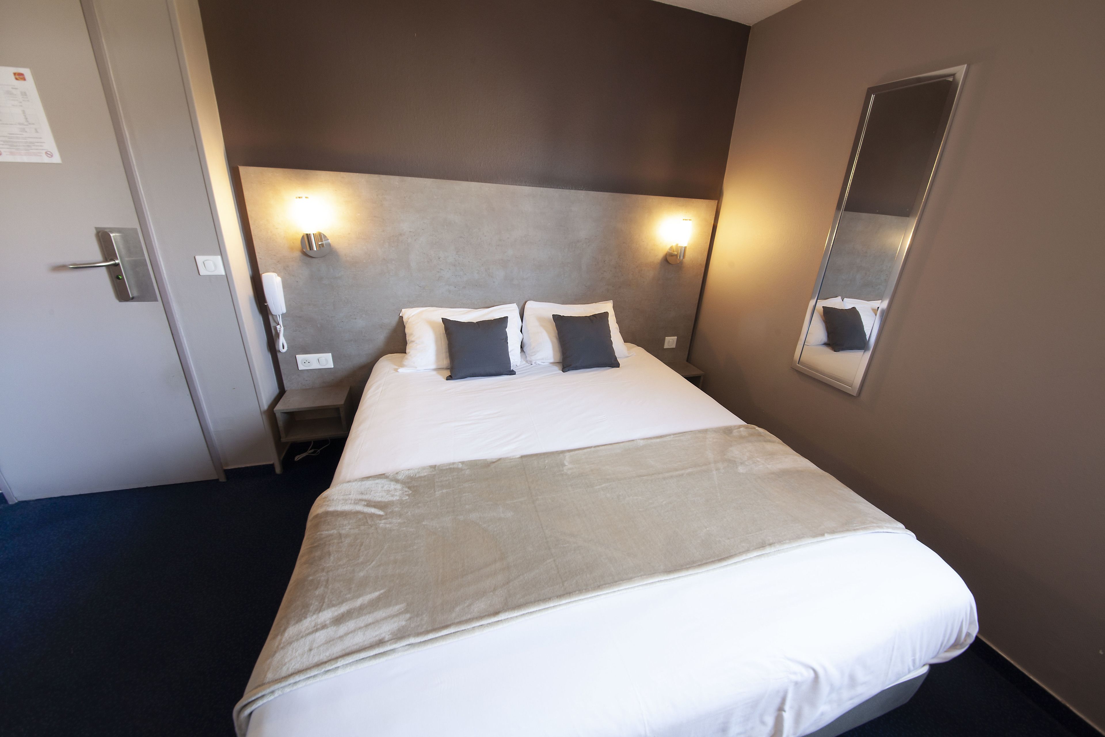 A hotel room with a large bed, two bedside lamps, a mirror, and a door with a lock.