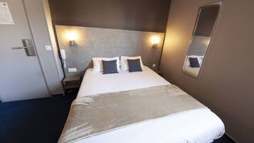A hotel room with a large bed, two bedside lamps, a mirror, and a door with a lock.