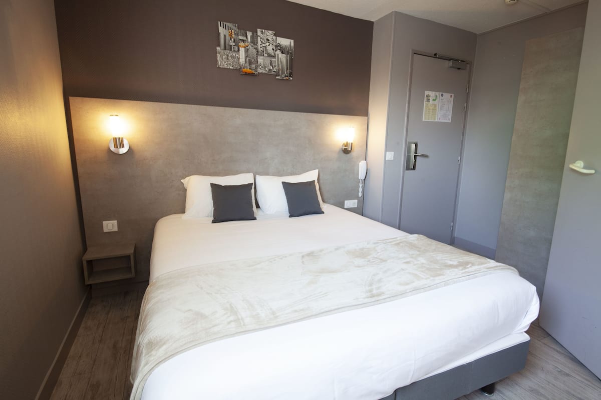 Une chambre d’hôtel avec un grand lit, deux lampes de chevet, une petite table de nuit et une porte dotée d’une serrure et d’un calendrier.