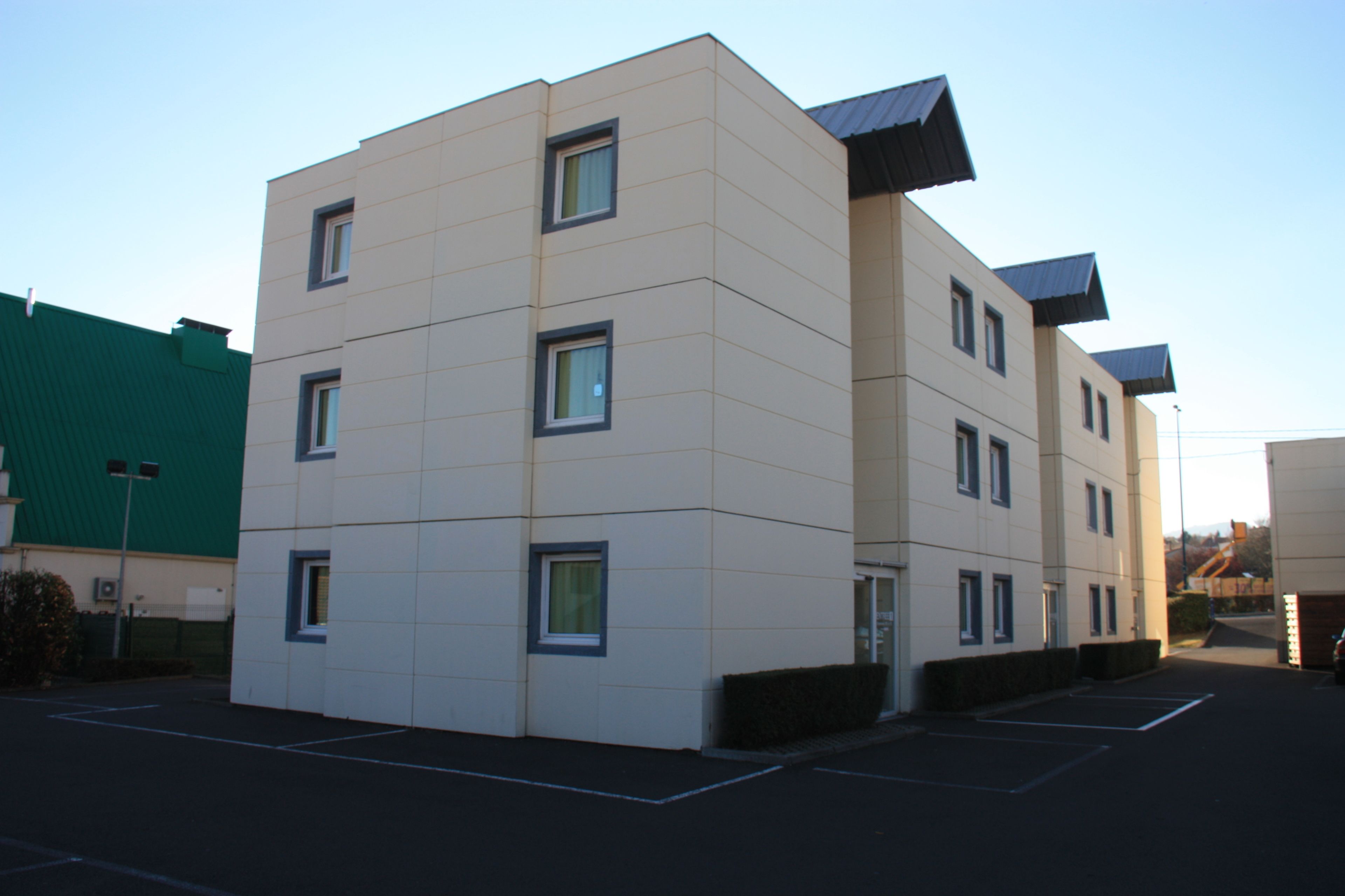 A multi-story building with a flat facade, rectangular windows, and a parking lot in front.