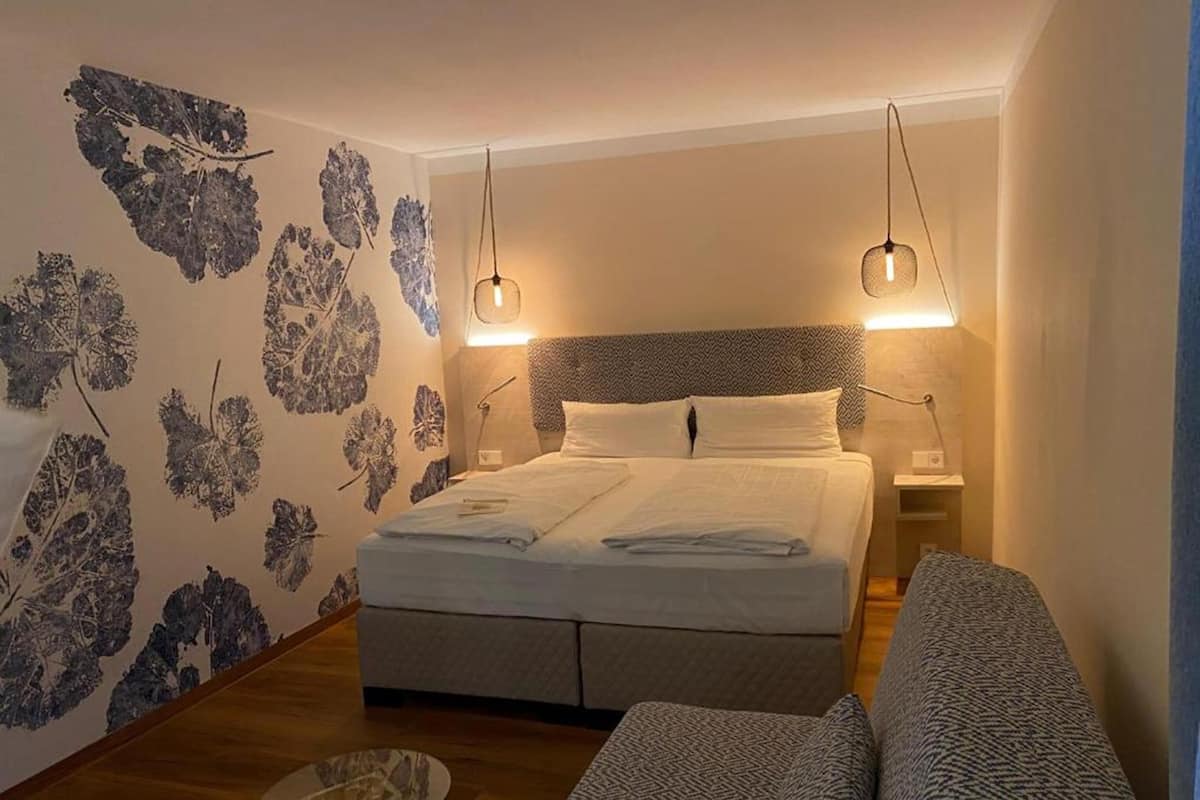 A bedroom with a bed, two bedside tables, a sofa, and a patterned wall.