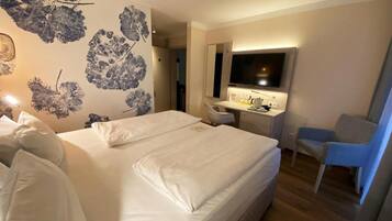Habitación de hotel con una cama grande, un escritorio con silla, televisor y pared con estampado floral.