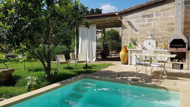A pool area with a stone wall, outdoor seating, and a pizza oven. - B&B Masseria 12 Granai (Minervino di Lecce)