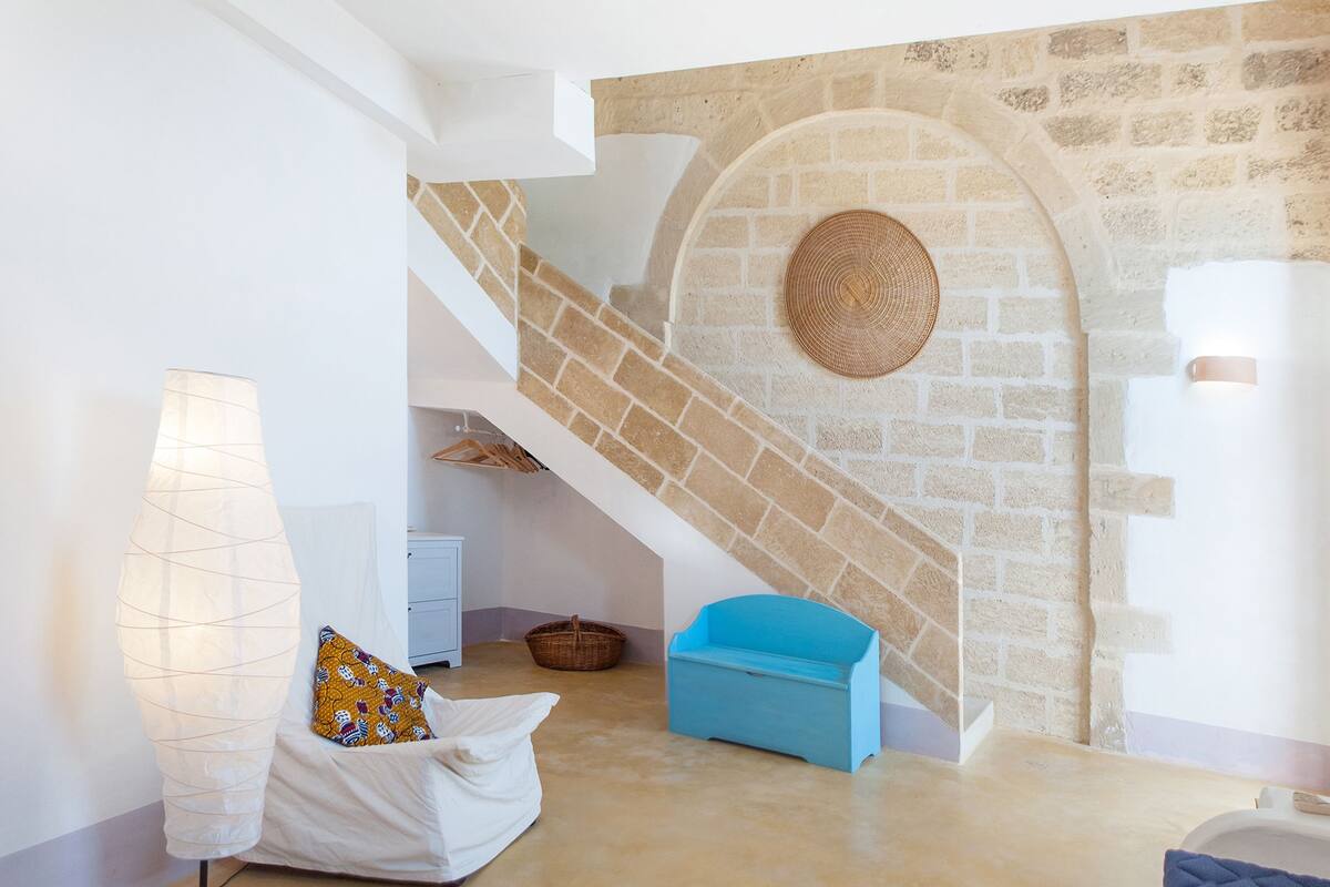 A modern interior with a stone wall, a staircase, a blue bench, a white sofa, and a lamp.