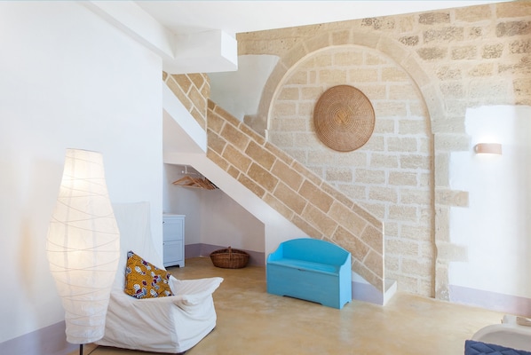 A modern interior with a stone wall, a staircase, a blue bench, a white sofa, and a lamp.