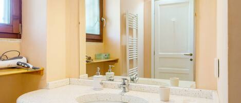 A bathroom with a white speckled sink, two faucets, a mirror, and a towel rack.
