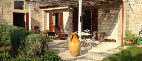 Un patio cubierto al aire libre con un edificio rústico de piedra, un jarrón grande y mobiliario exterior.