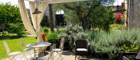 An outdoor patio area with a round table and chairs, surrounded by lush greenery and a pergola structure.