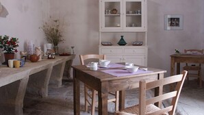 A rustic dining area with a wooden table and chairs, a white cabinet with glass doors, and a stone floor. - B&B Masseria 12 Granai (Minervino di Lecce)