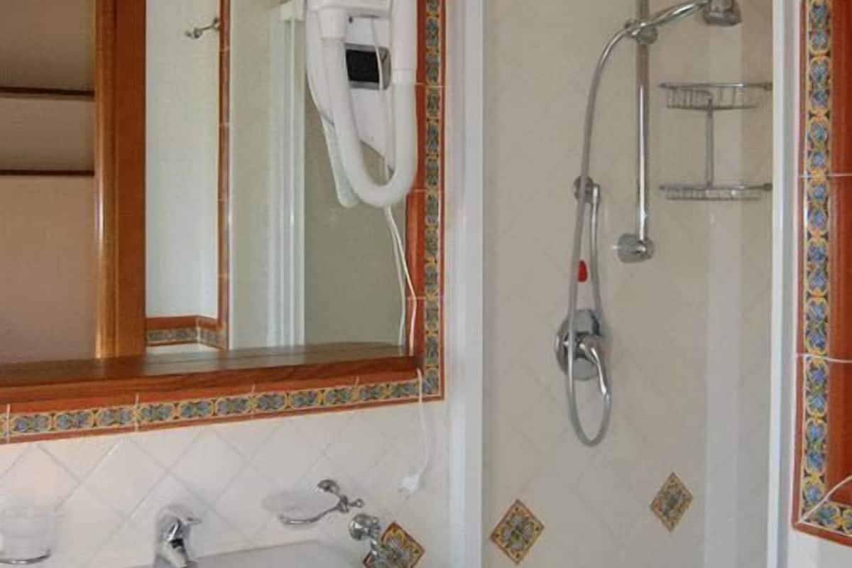 A bathroom with a sink, mirror, hairdryer, and shower.