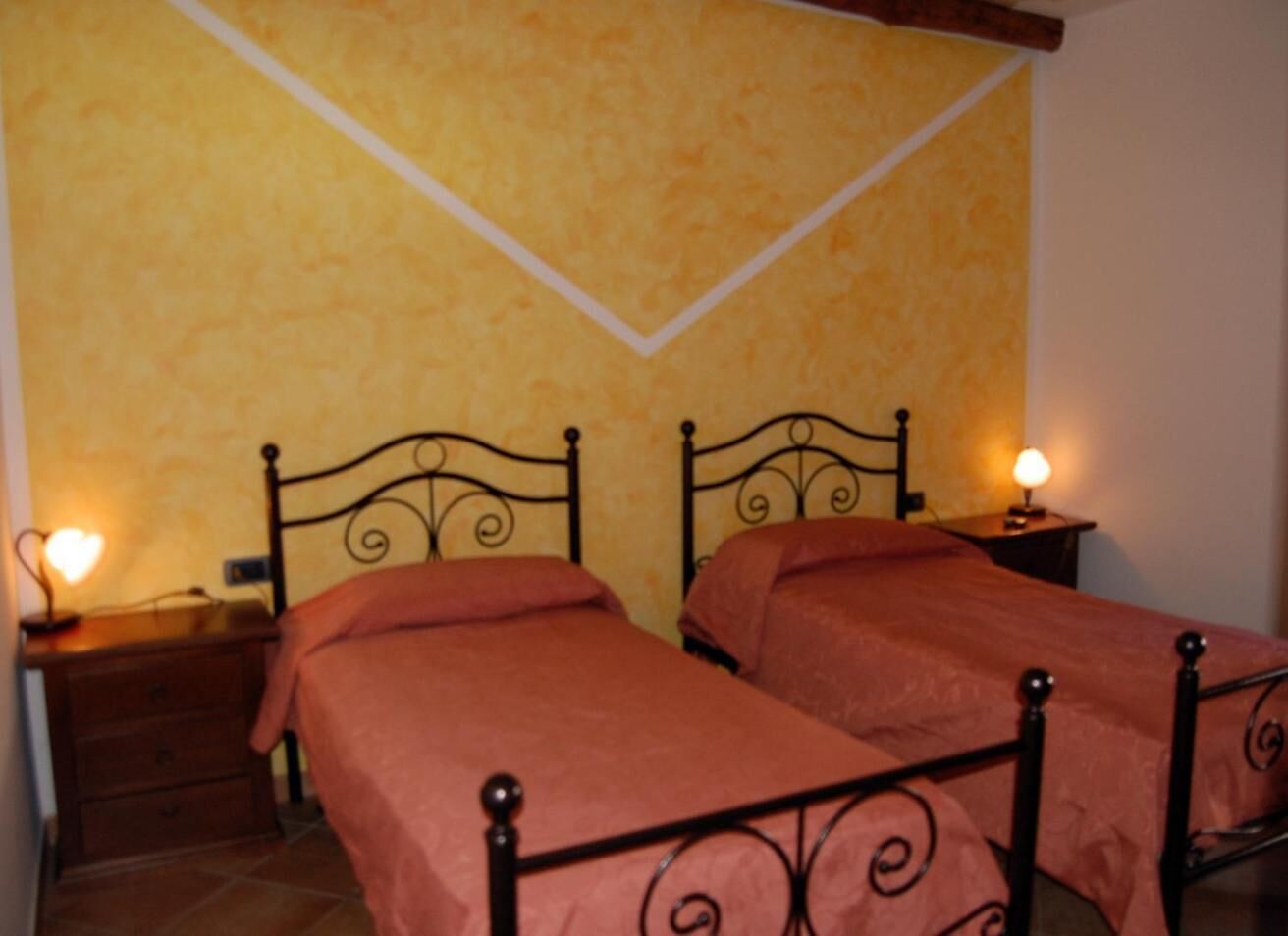 A room with two beds, each with a headboard and a bedside table with a lamp.