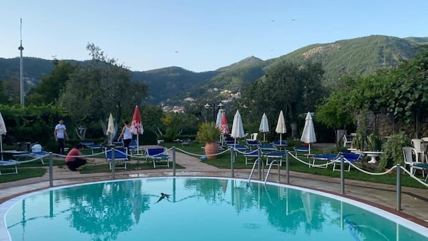 Piscina com espreguiçadeiras e guarda-sóis, rodeada por vegetação e colinas.