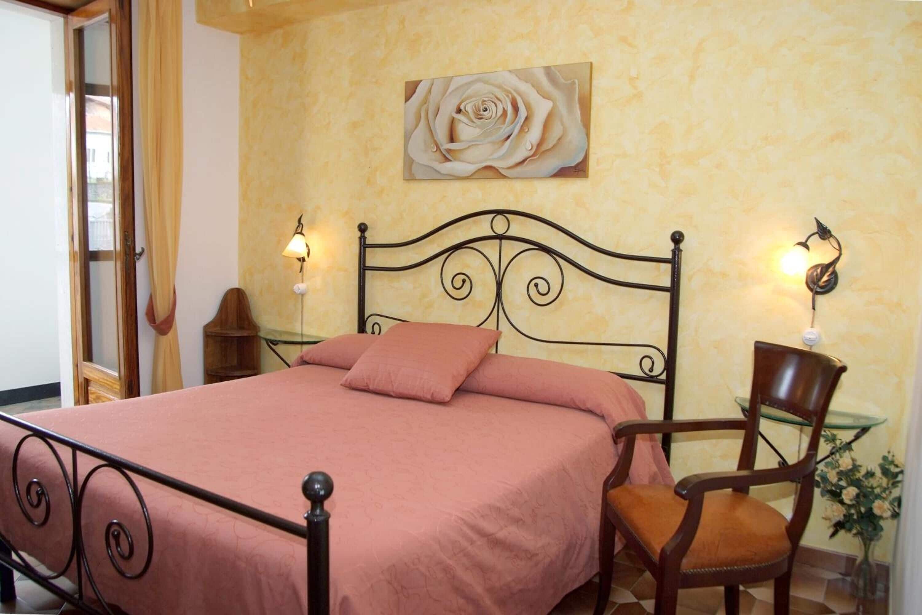 Ein Schlafzimmer mit Bett, Stuhl, Nachttisch, Lampe und einem Bild an der Wand.