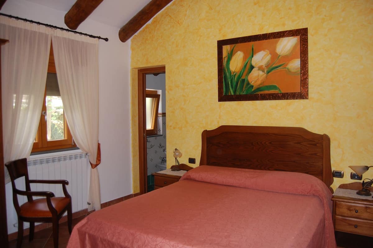 A bedroom with a wooden bed, a chair, a nightstand, and a painting on the wall.