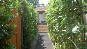Um estreito caminho de jardim leva a uma porta de madeira e a um pequeno espaço de estar ao ar livre.