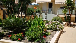Un edificio residencial con balcón, mobiliario exterior y un jardín con diversas plantas y flores.