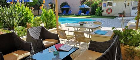 An outdoor patio area with wicker furniture, a pool, and various plants.