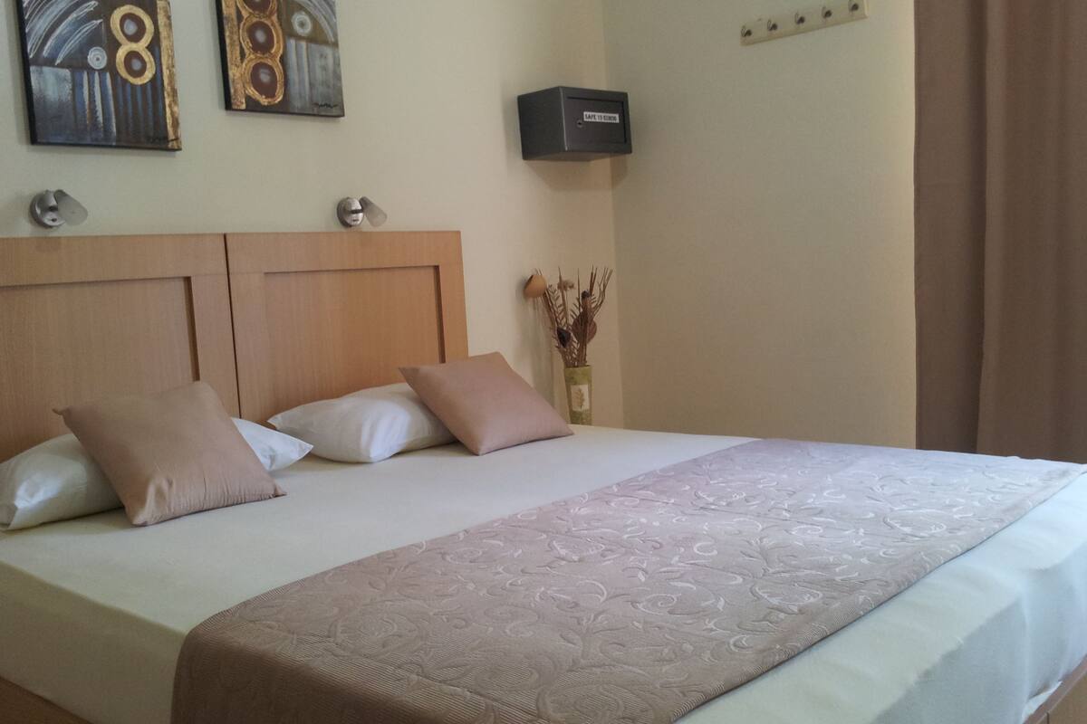 A neatly made bed with a wooden headboard, two pillows, and a decorative bedside table with a vase of dried plants.