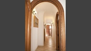 A hallway with a tiled floor, wooden arches, and wall-mounted lighting fixtures. - Villa Palumbo (Positano)