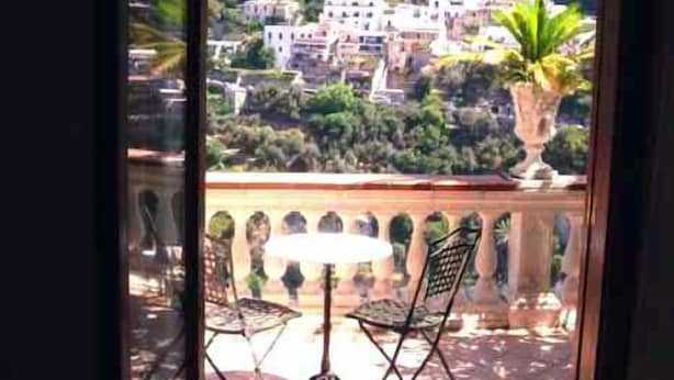 A balcony with a view of a hillside village, a potted plant, and two chairs. - Villa Palumbo (Positano)