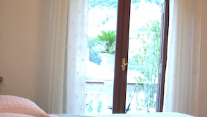 A bedroom with a bed, a wooden door, and a view of greenery outside. - Villa Palumbo (Positano)