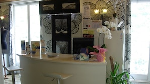 A reception area with a white counter, a bar stool, a potted plant, and decorative wall panels. - Villa Palumbo (Positano)
