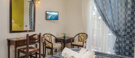 A room with a bed, a desk, two chairs, a mirror, a television, and a window with curtains.