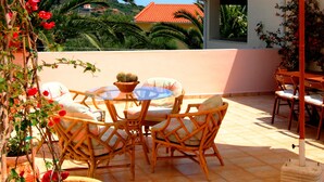 Un patio al aire libre con mesa y sillas, un paraguas grande y una maceta con flores rojas.