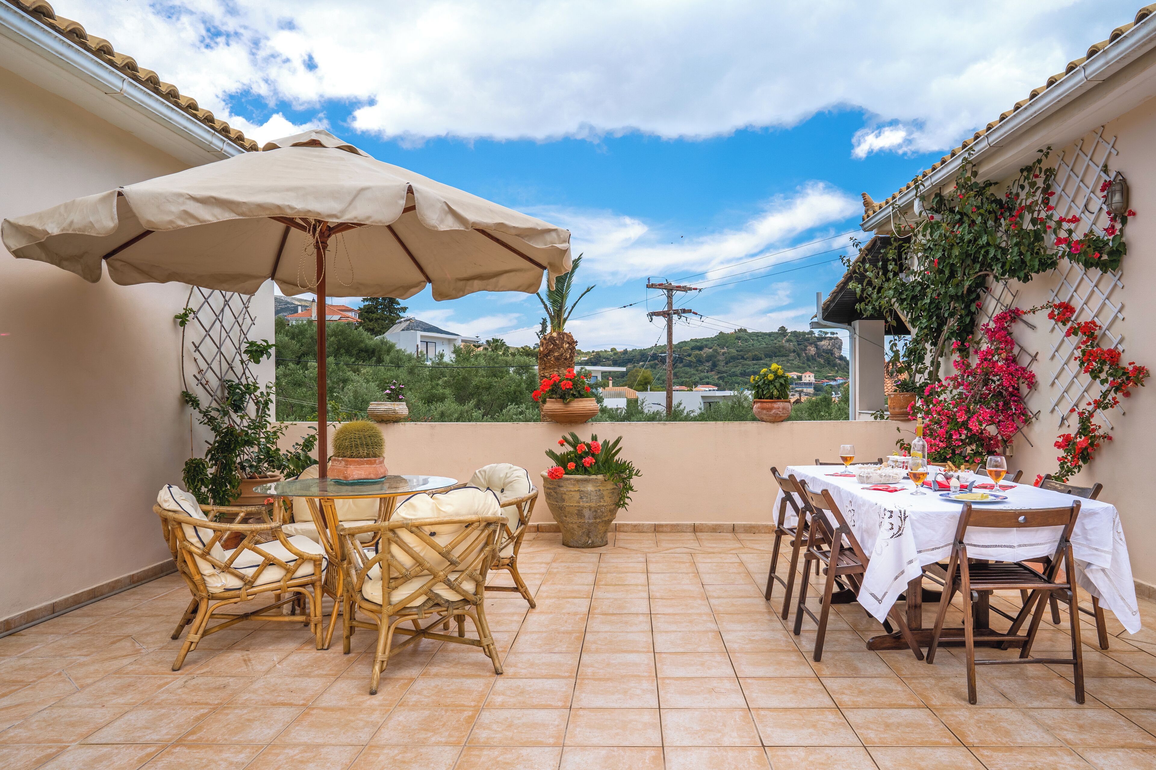 Une terrasse extérieure avec une table et des chaises, un grand parasol et des plantes en pot.