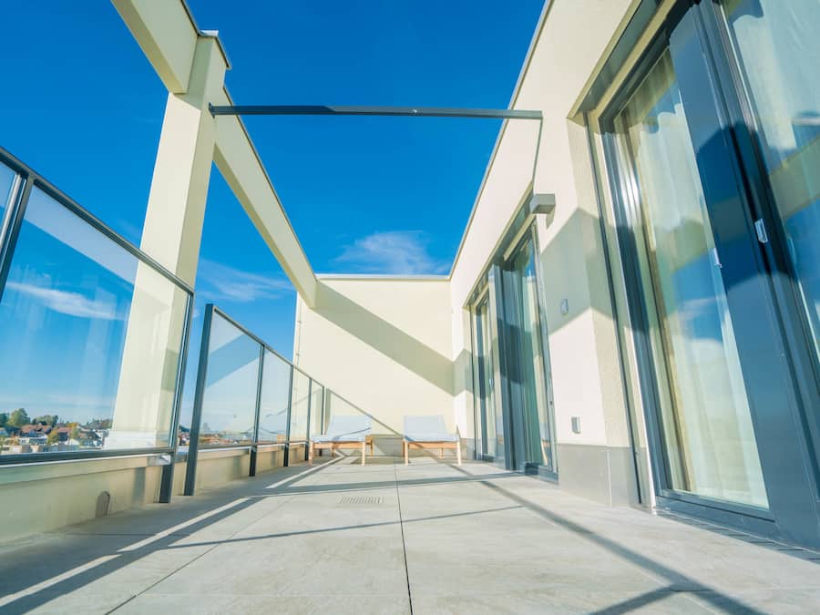 Un edificio moderno con amplios ventanales y un balcón con dos sillones de relax.