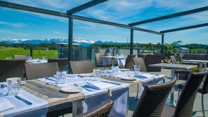 An outdoor dining area with tables and chairs, overlooking a mountainous landscape. - Hotel Swiss Star (Wetzikon)