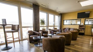 A spacious lounge area with leather sofas, a coffee table, and a bar area. Large windows offer a view of the cityscape. - Hotel Swiss Star (Wetzikon)