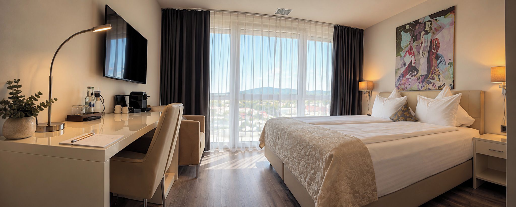 A hotel room with a bed, a desk, a chair, a television, and a painting on the wall.