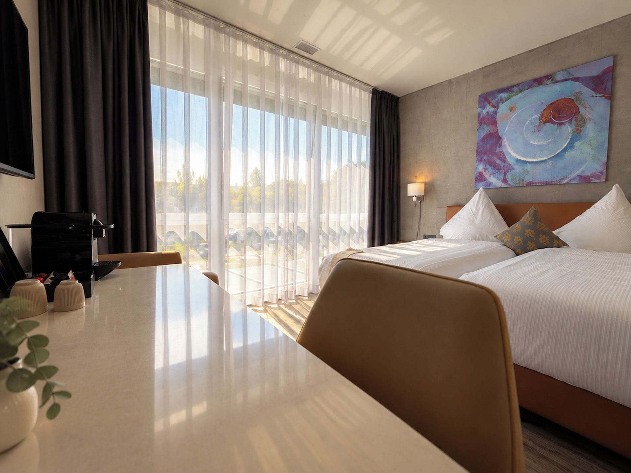 Ein Hotelzimmer mit einem Bett, einem Schreibtisch, einem Stuhl, einer Kaffeemaschine und einem Bild an der Wand.