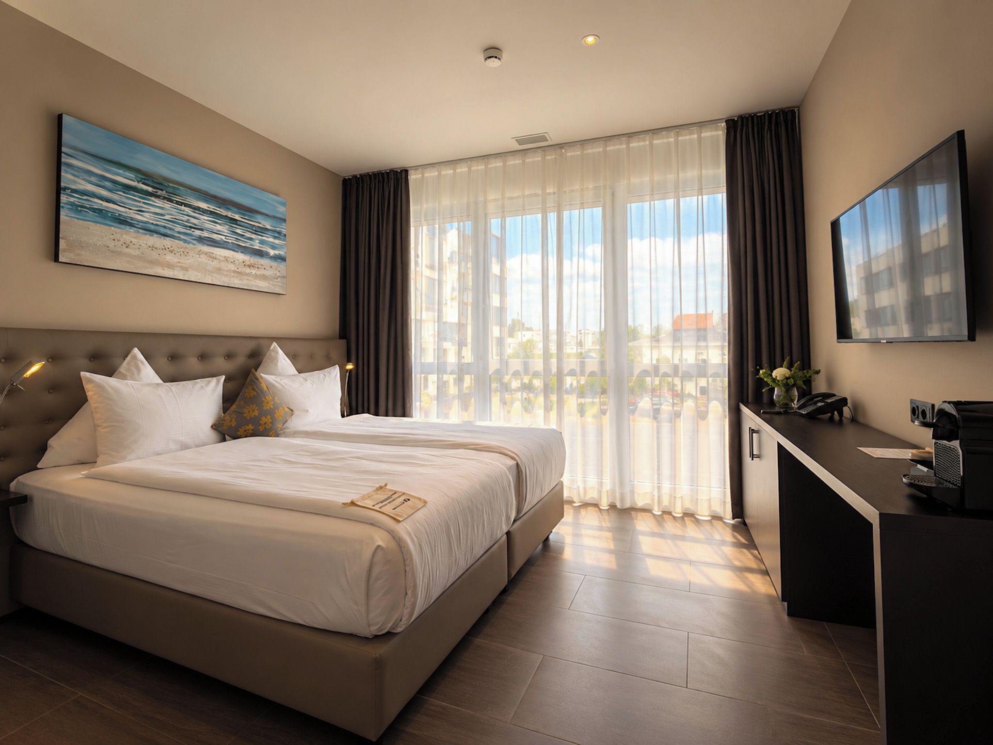 A hotel room with a large bed, a desk, a TV, and a window with curtains.