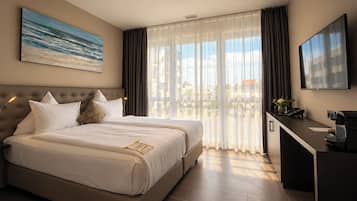 A hotel room with a large bed, a desk, a TV, and a window with curtains.