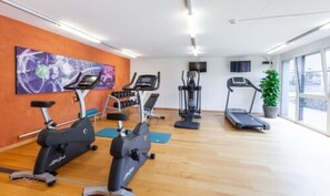 Un gimnasio con máquinas de cardio, mancuernas y una cinta de correr.
