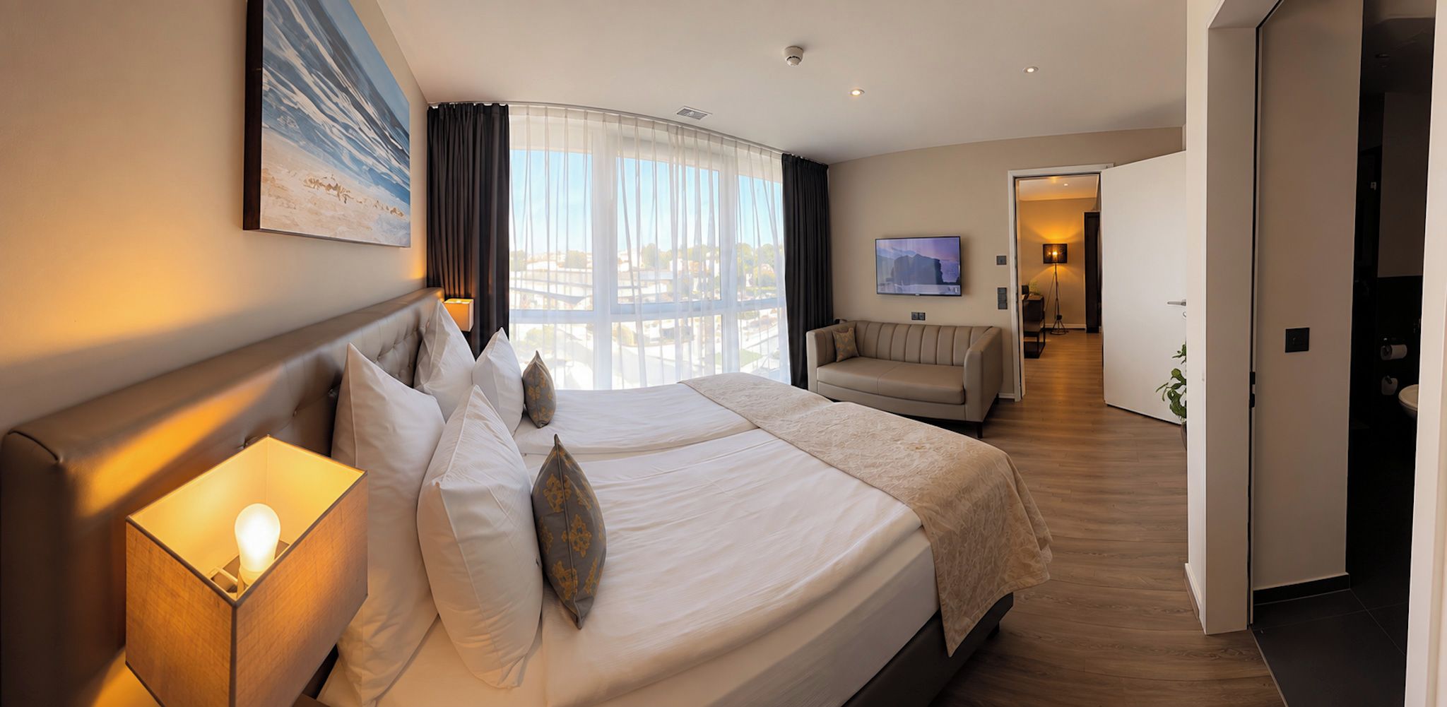 A hotel room with two beds, a large window, a sofa, and a television.