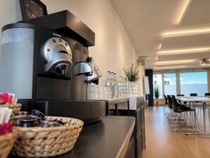 A modern coffee machine in a well-lit room with a long table and chairs, suggesting a cafe or meeting area. - Hotel Swiss Star (Wetzikon)