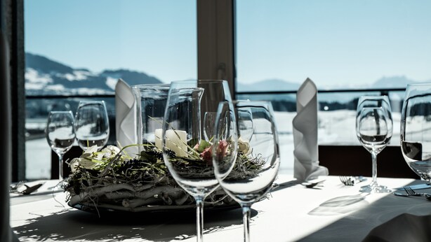 A table set for dining with wine glasses and a centerpiece of flowers and greenery, overlooking a mountainous landscape. - Hotel Swiss Star (Wetzikon)