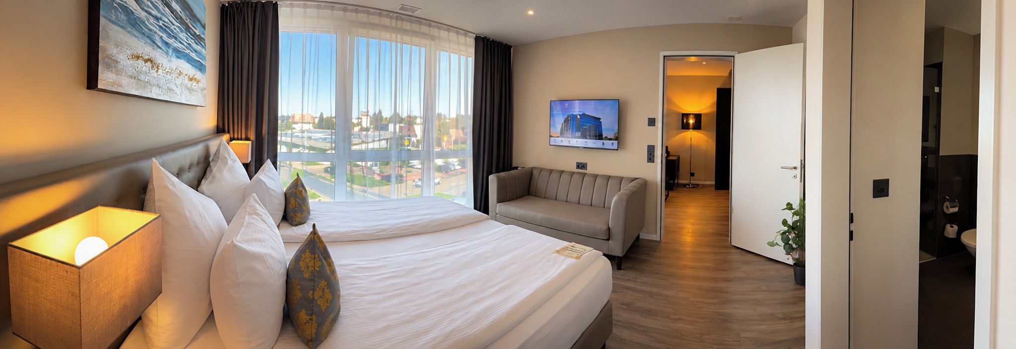 Habitación de hotel con una cama grande, un sofá, un televisor y vistas a la ciudad.