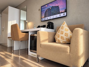 A modern hotel room with a sofa, a desk, and a television displaying a hotel image. - Hotel Swiss Star (Wetzikon)