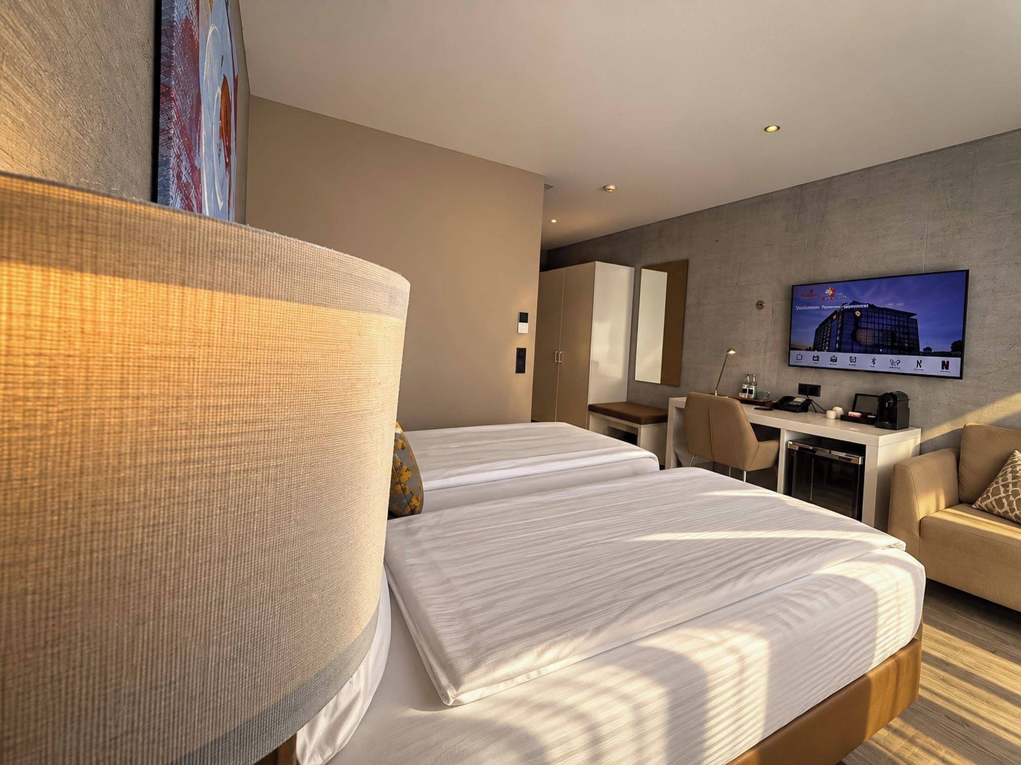 A hotel room with two beds, a desk, a chair, a television, and a large painting on the wall.