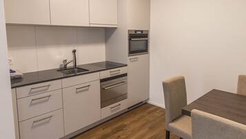 A modern kitchen with white cabinets, a black countertop, and a wooden dining table with chairs.