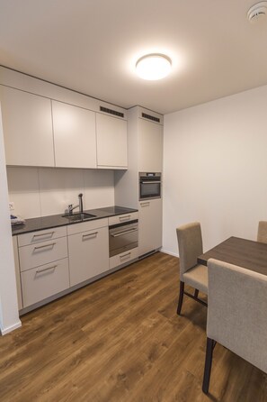 Una cocina moderna con armarios blancos, encimera negra y una mesa de comedor de madera con sillas.